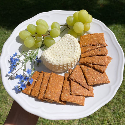 Plate of Smoked Paprika crackers with green grapes, a round of fresh white cheese and small blue flowers