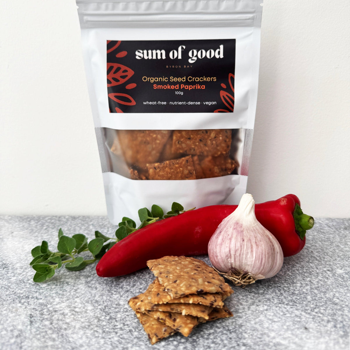 Bag of Sum of Good Smoked Paprika crackers with a stack of crackers, a long red pepper, garlic and oregano